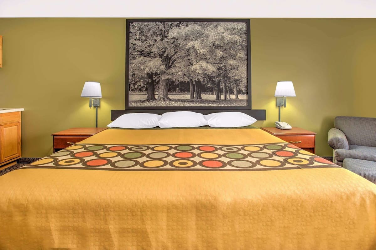 A hotel room with a bed, two bedside tables, a nightstand, a lamp, a chair, and a framed picture on the wall.