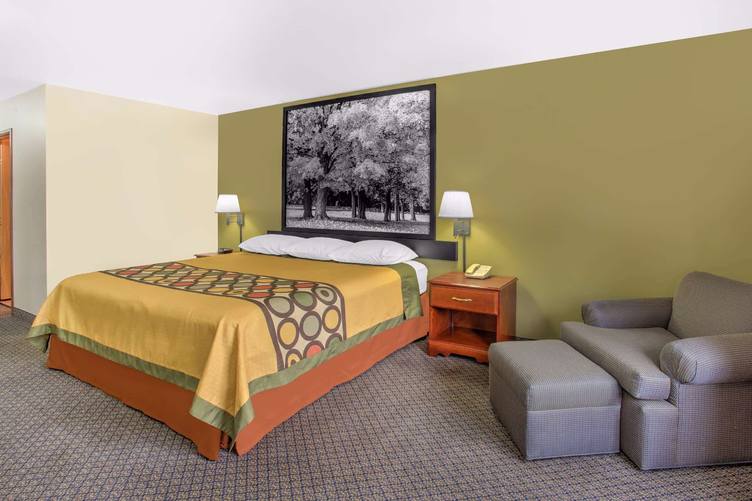 A hotel room with a bed, a chair, a nightstand, and a wall-mounted lamp.