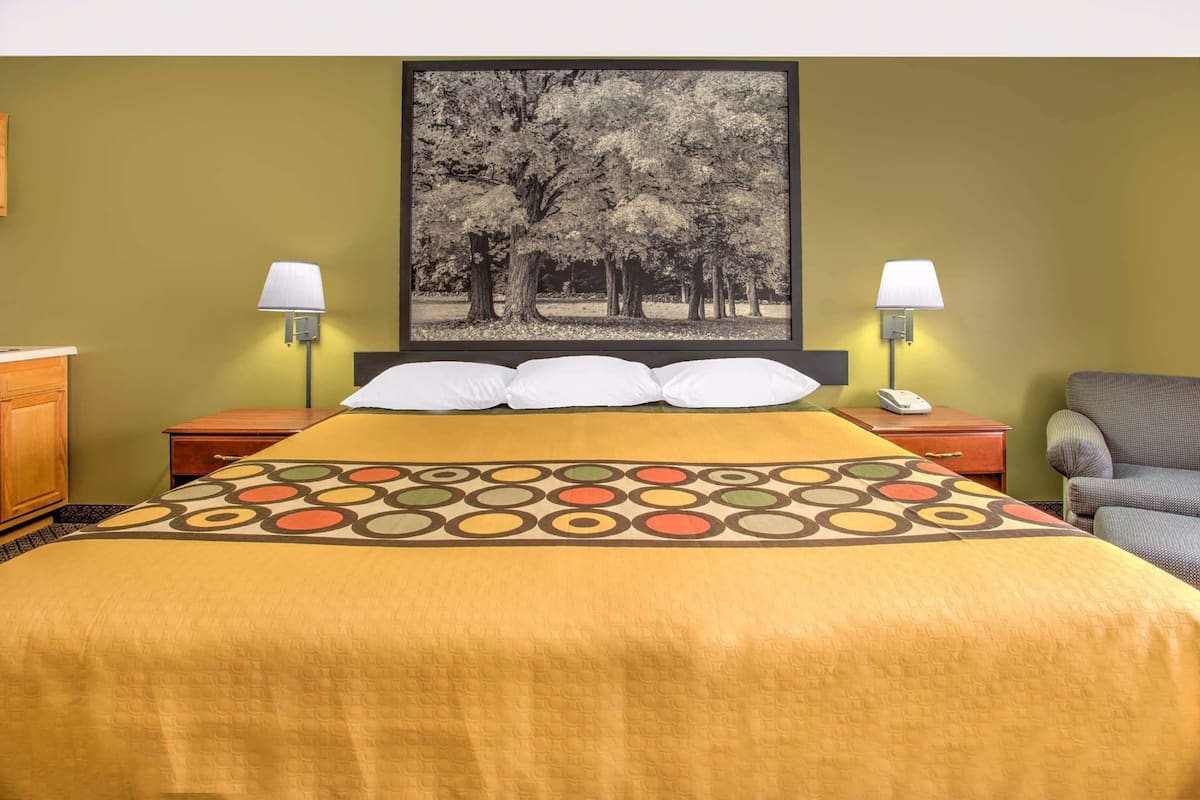 A hotel room with a bed, two bedside lamps, a nightstand, a chair, and a framed picture on the wall.