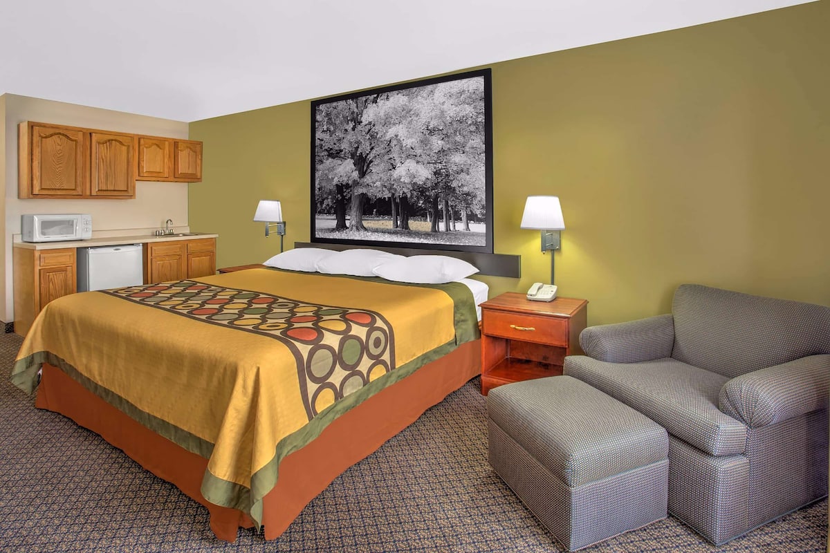 A hotel room with a bed, a desk with a microwave, a chair, and a large framed picture on the wall.