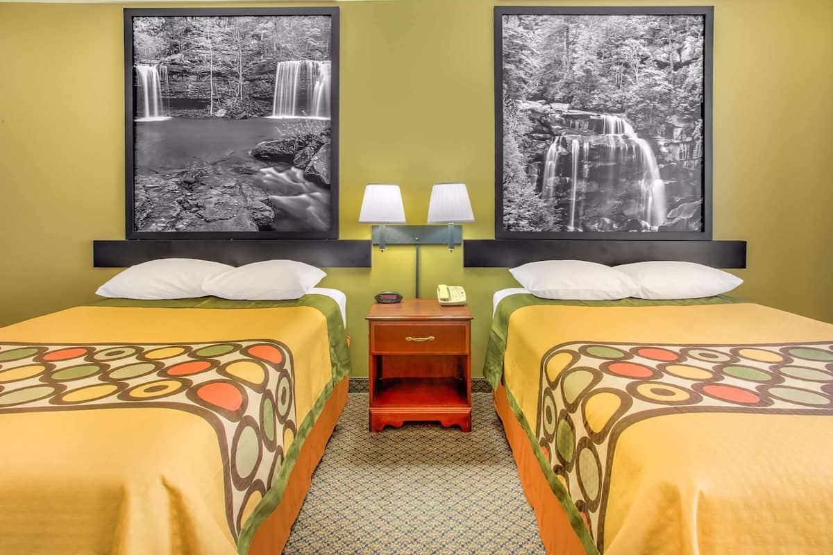 A hotel room with two beds, a nightstand with a lamp, and two framed black and white waterfall photographs on the wall.