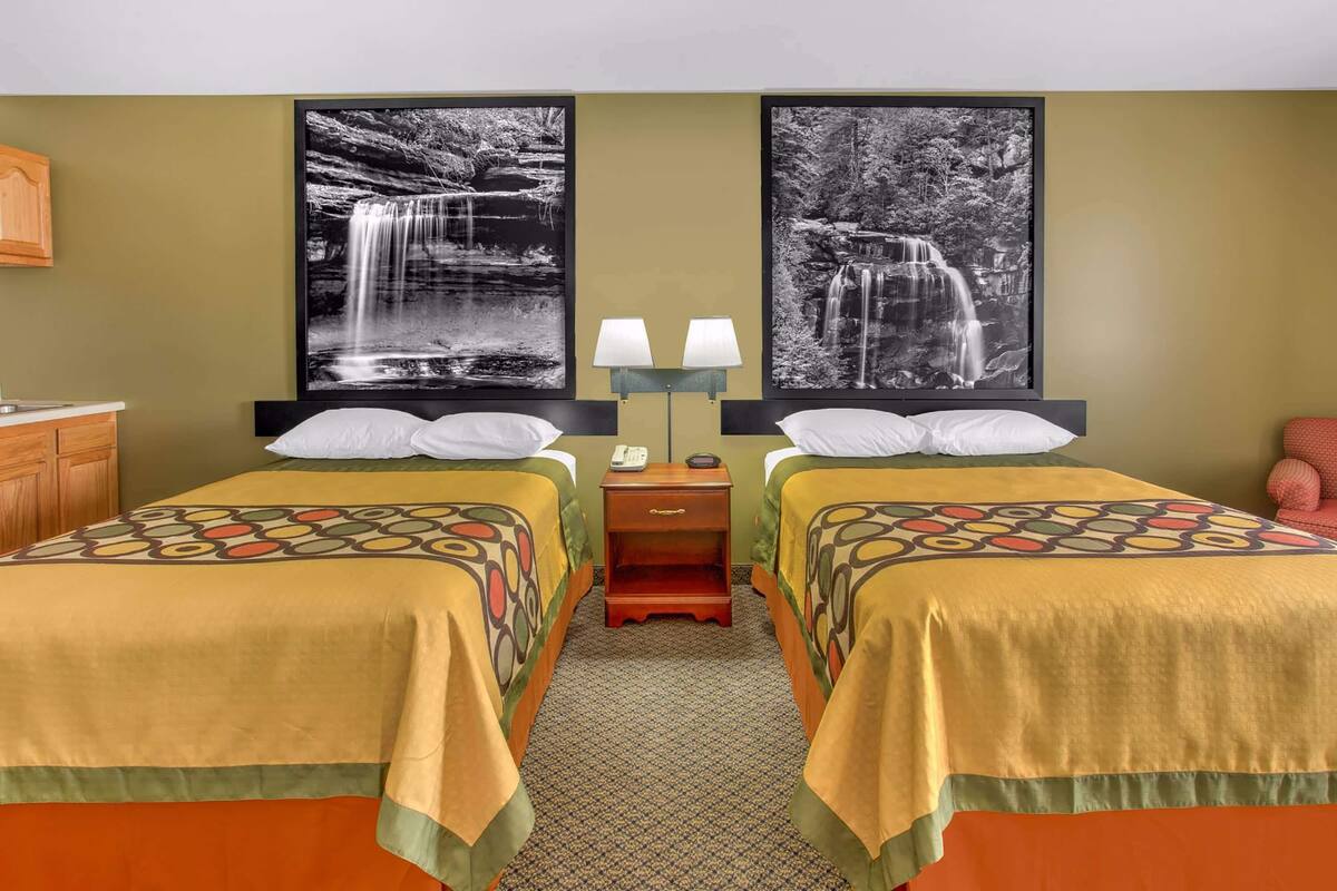 A hotel room with two beds, a nightstand, and two wall-mounted lamps.