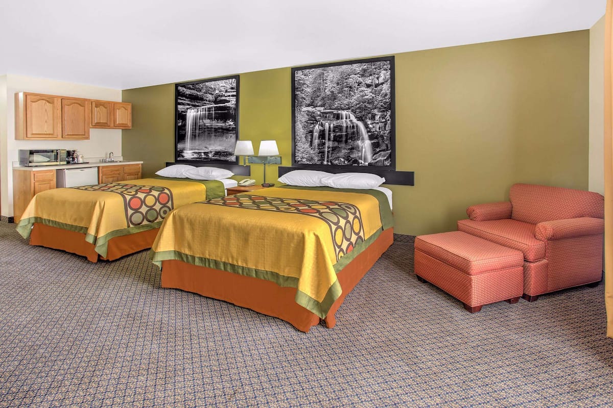 A hotel room with two beds, a kitchenette, and a red armchair.