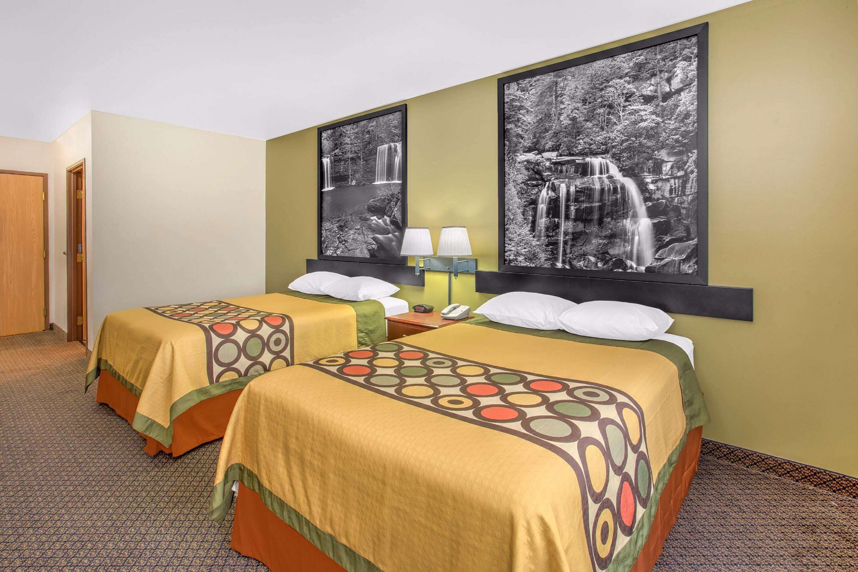A hotel room with two beds, each with a patterned bedspread, a nightstand with a lamp, and two framed black and white waterfall photographs on the wall.
