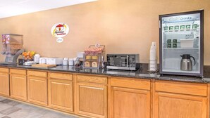 Zona de desayuno de hotel con cafetera, microondas y refrigerador lleno de bebidas frías.