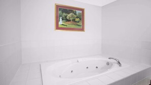 Un baño moderno con una bañera blanca grande, paredes de azulejos blancos y un cuadro enmarcados con una escena de jardín.