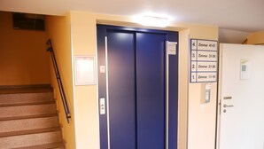 An elevator with a blue interior, a stairwell to the left, and a door to the right with room numbers. - Parkhotel Marzahn (Berlin)