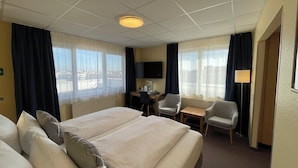A hotel room with two beds, a desk, two chairs, a TV, and large windows with curtains. - Parkhotel Marzahn (Berlin)