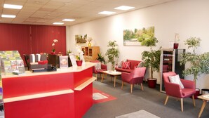 A reception area with a red desk, multiple chairs, potted plants, and a painting on the wall. - Parkhotel Marzahn (Berlin)