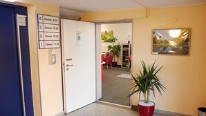 A hotel lobby with a reception desk, a directory on the wall, and a potted plant. - Parkhotel Marzahn (Berlin)