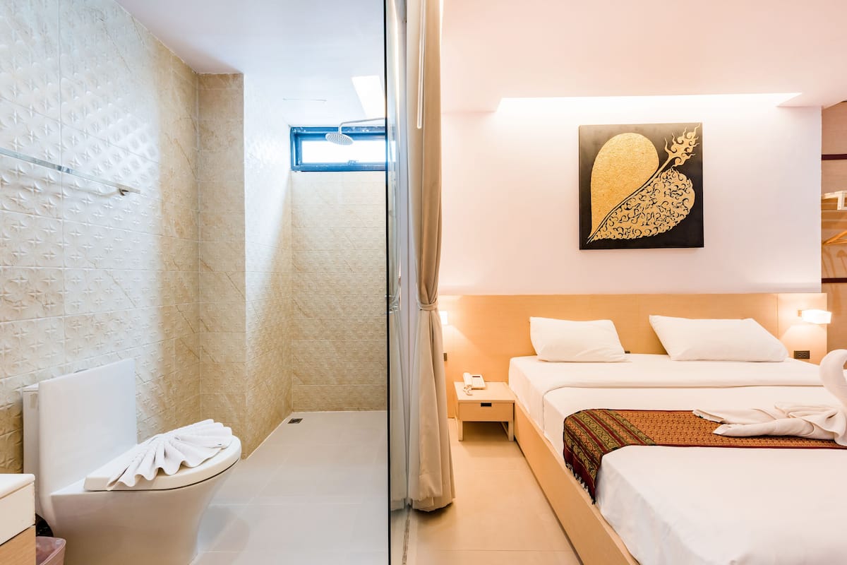 A bathroom with a shower, toilet, and a sink. There is a bed with white bedding and a decorative wall piece.