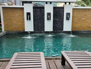 Une piscine agrémentée de jeux d’eau, dotée d’une terrasse en bois et de chaises longues.
