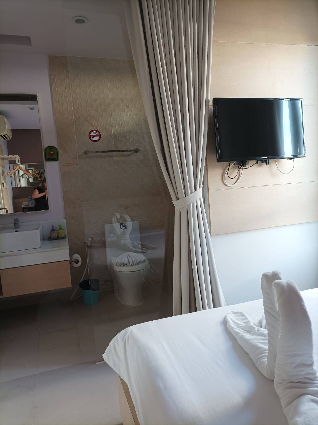 A hotel room with a bed, a TV mounted on the wall, a bathroom with a toilet, and a shower.