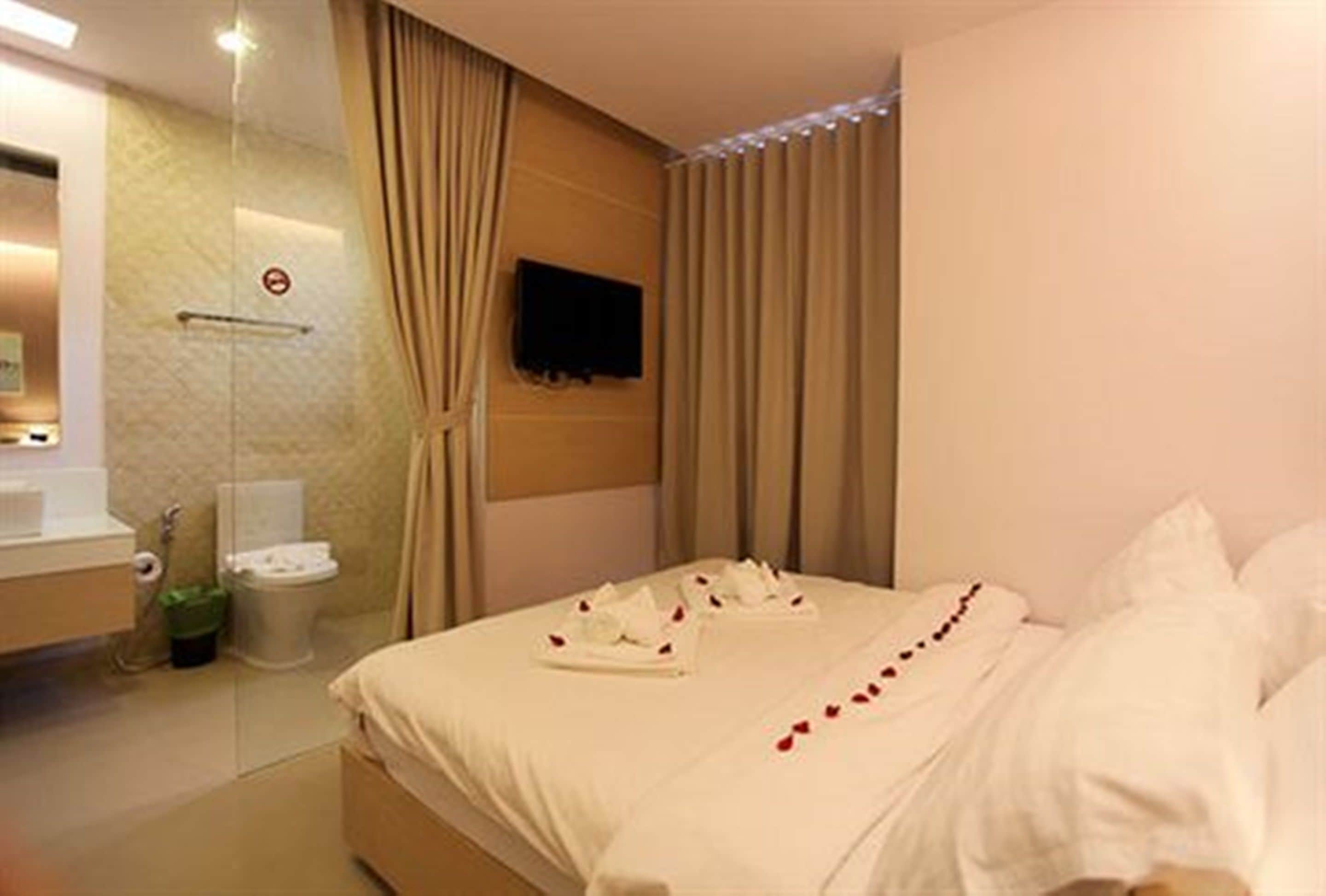 A hotel room with a bed, a TV mounted on the wall, a bathroom with a toilet and sink, and a shower area.