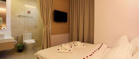 A hotel room with a bed, a TV mounted on the wall, a bathroom with a toilet and sink, and a shower area.