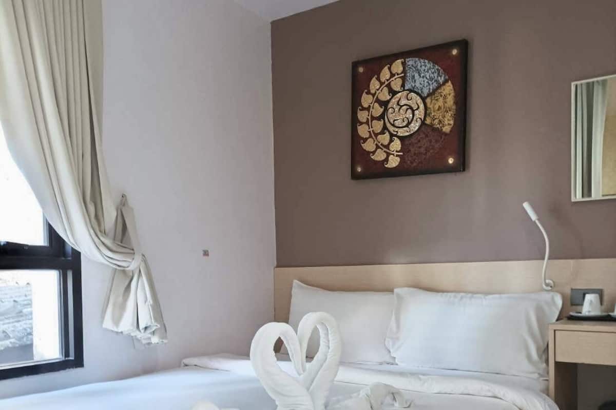 A neatly made bed with white linens and two swan-shaped towels.