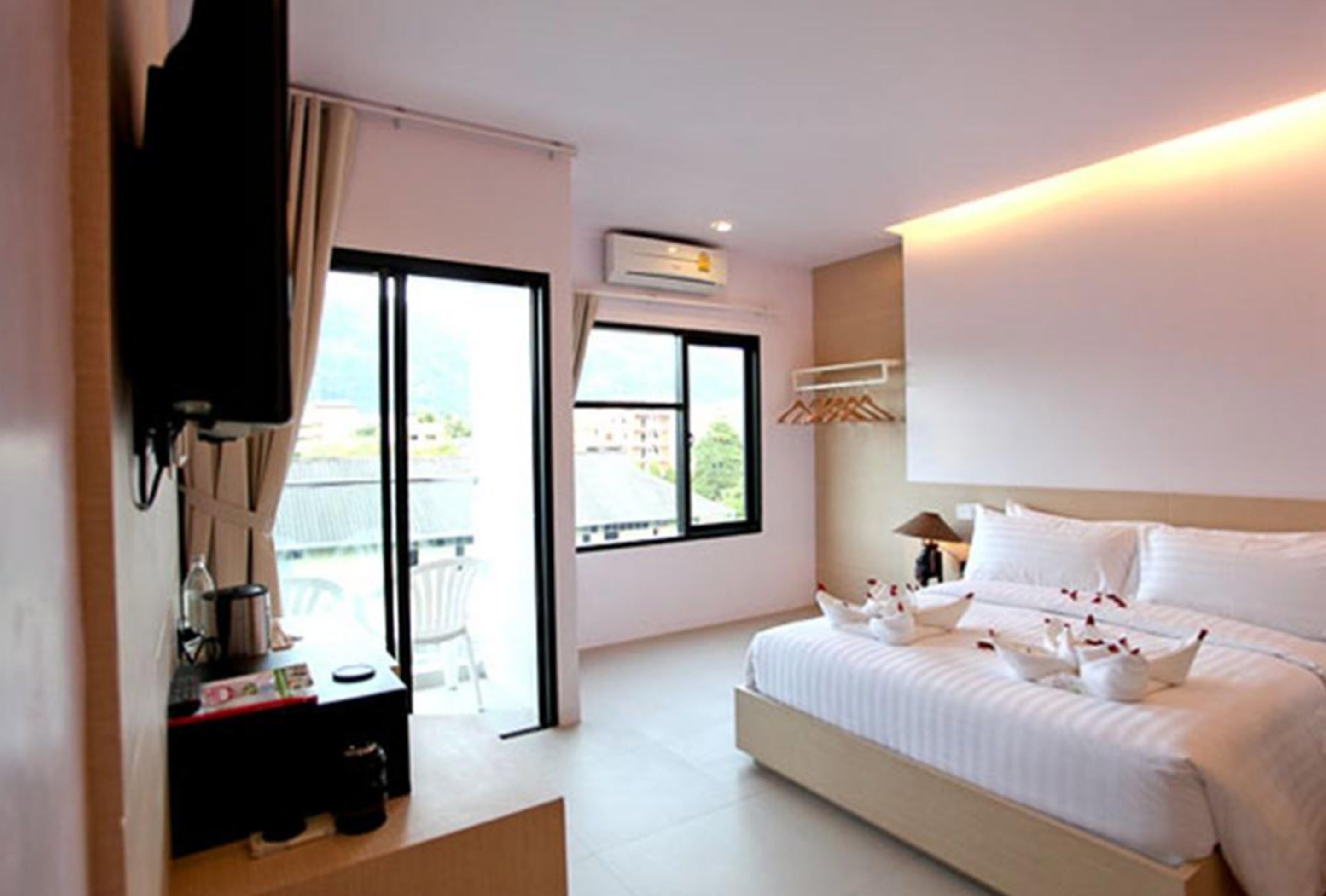 A hotel room with a bed, a TV, a desk with a chair, and a balcony with a view.