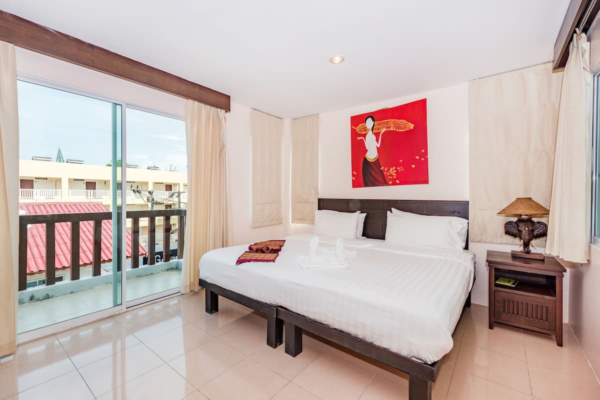 A hotel room with a large bed, a nightstand, a wall-mounted lamp, and a balcony with a view of the building's exterior.