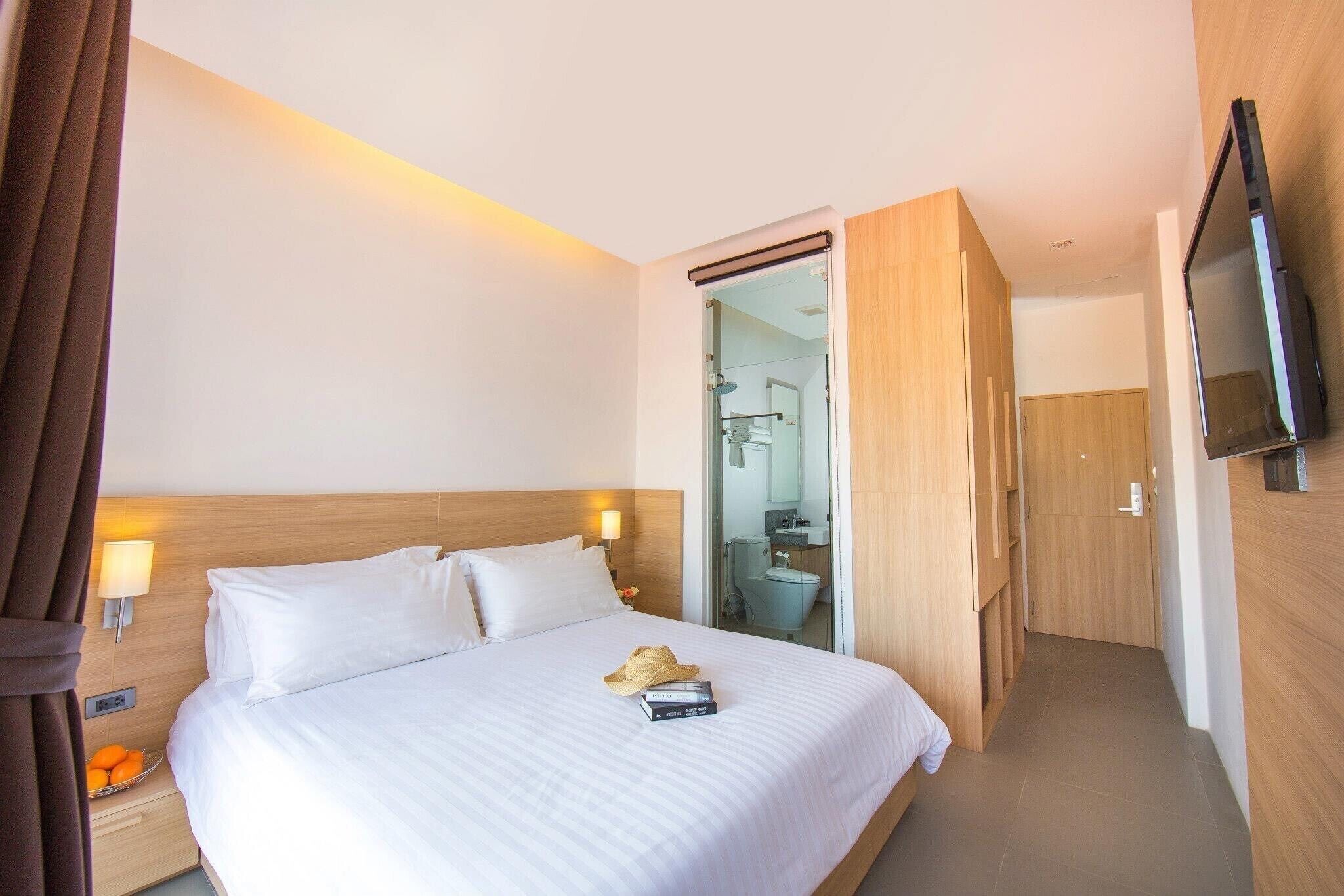 A hotel room with a large bed, bedside lamps, a TV, and a bathroom visible through an open door.