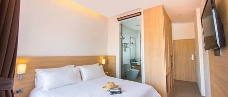A hotel room with a large bed, bedside lamps, a TV, and a bathroom visible through an open door.