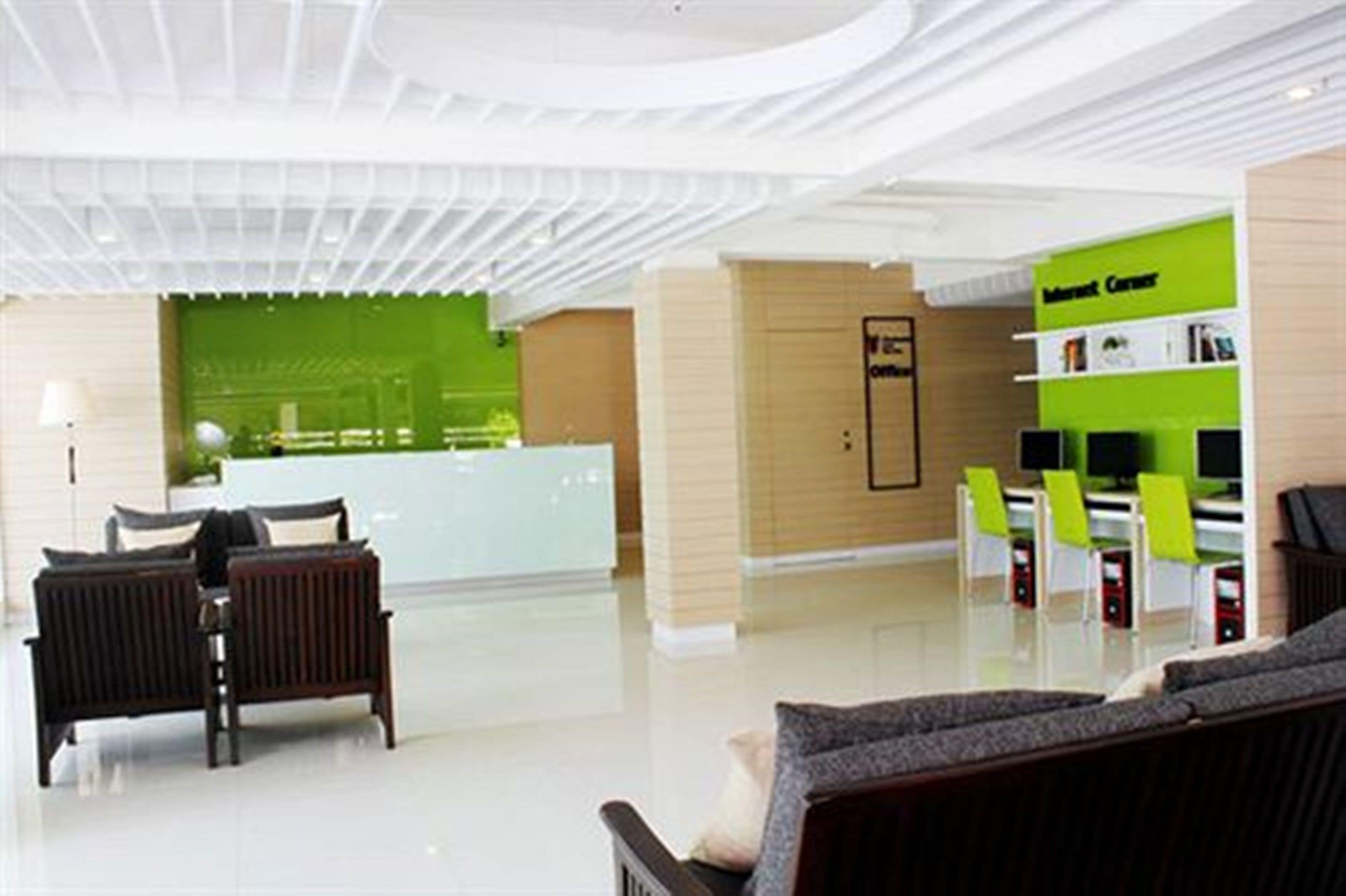 A modern lobby with a reception desk, seating area, and a green information counter.