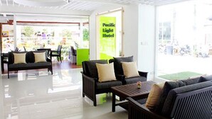 Un hall d'hôtel comprenant un comptoir d'accueil, un espace salon et une enseigne verte et lumineuse indiquant le nom de l'hôtel : Pacific Light Hotel.