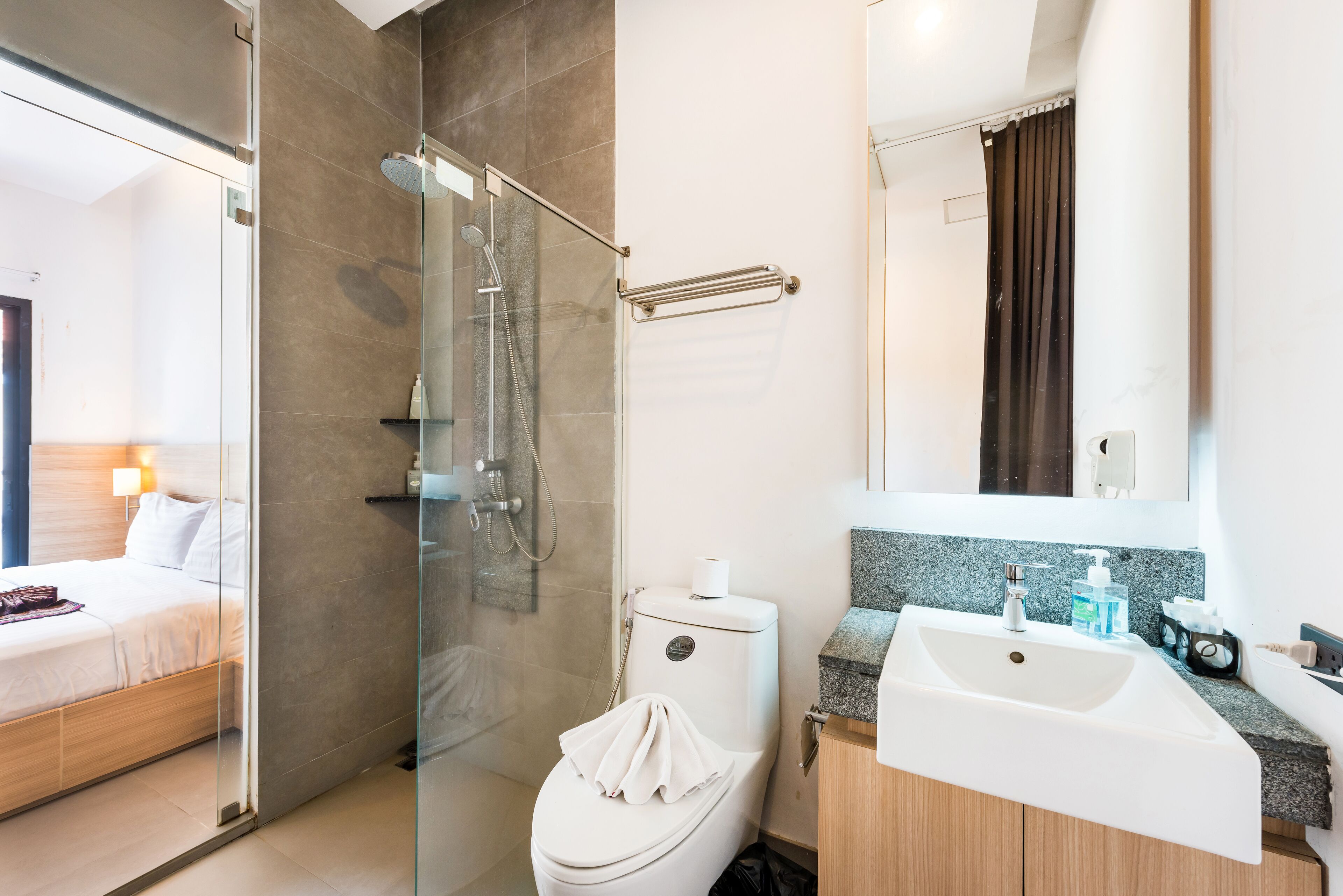 A modern bathroom with a glass shower enclosure, a white toilet, a sink with a soap dispenser, and a mirror above the sink.