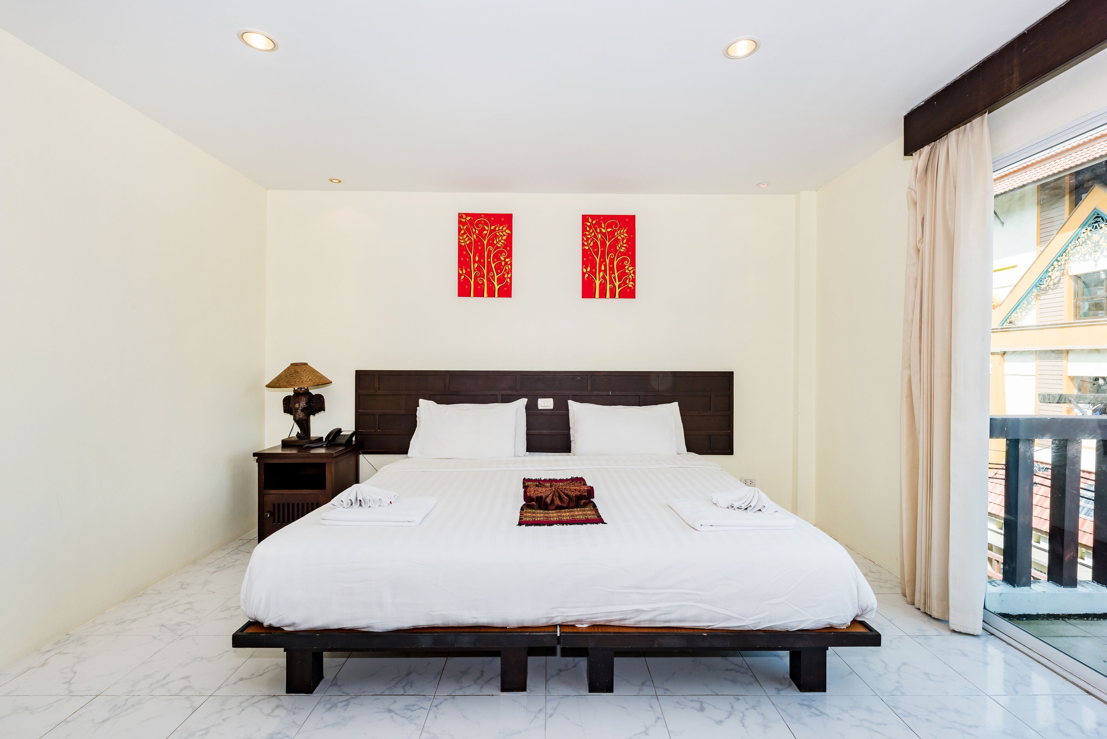 A hotel room with a large bed, a nightstand with a lamp, and two red decorative panels on the wall.