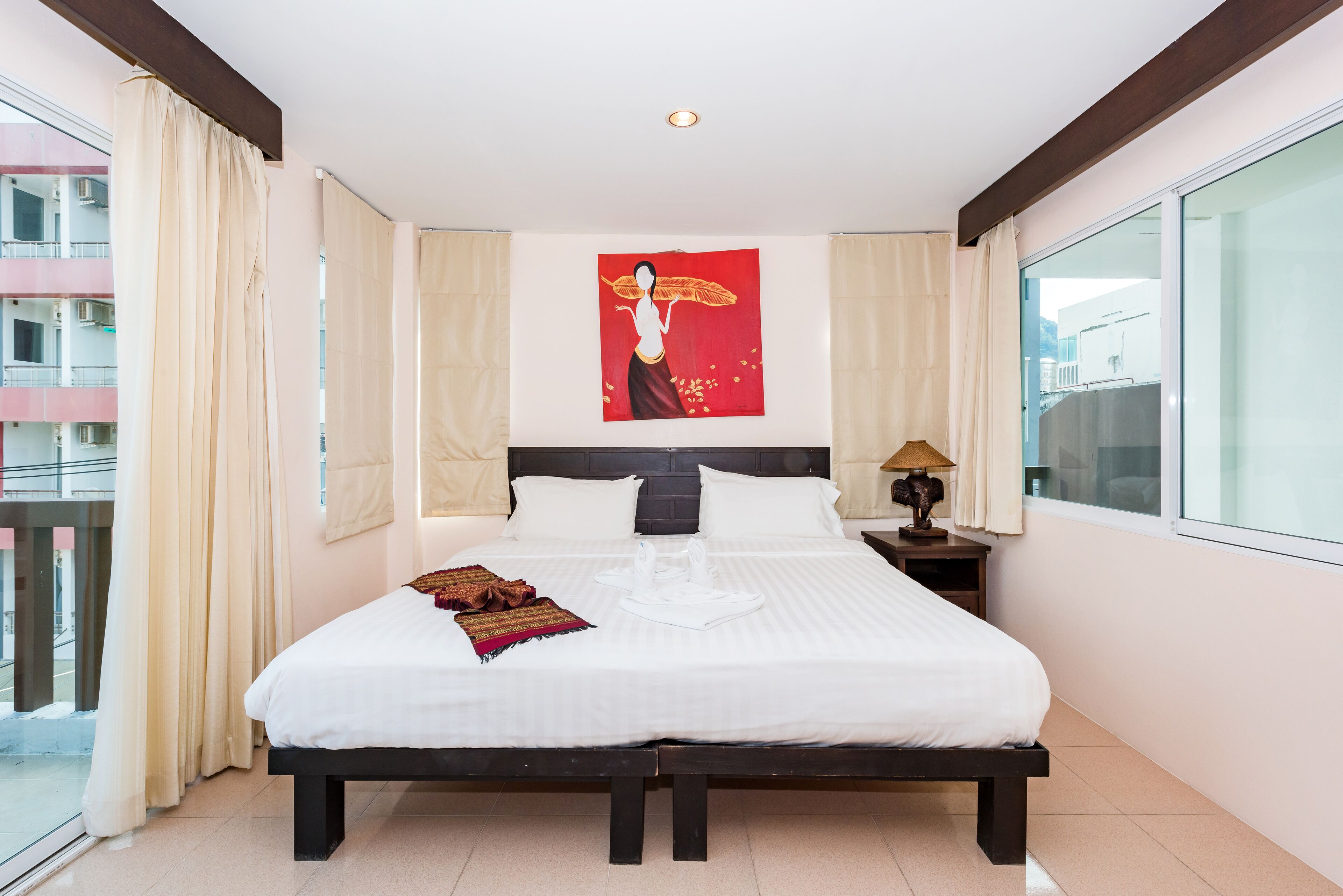 Une chambre d’hôtel avec un grand lit, une table de chevet avec une lampe, une fenêtre avec des rideaux et une œuvre d’art accrochée au mur.