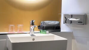 Un lavamanos con espejo, un dispensador de toallas y tres vasos de vidrio.