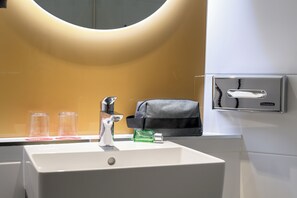A bathroom sink with a mirror, a towel dispenser, and three glass tumblers. - ibis Berlin Kurfürstendamm (Berlin)