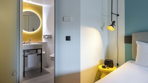 Una habitación de hotel moderna con baño, una mesita de noche con lámpara y una cama.