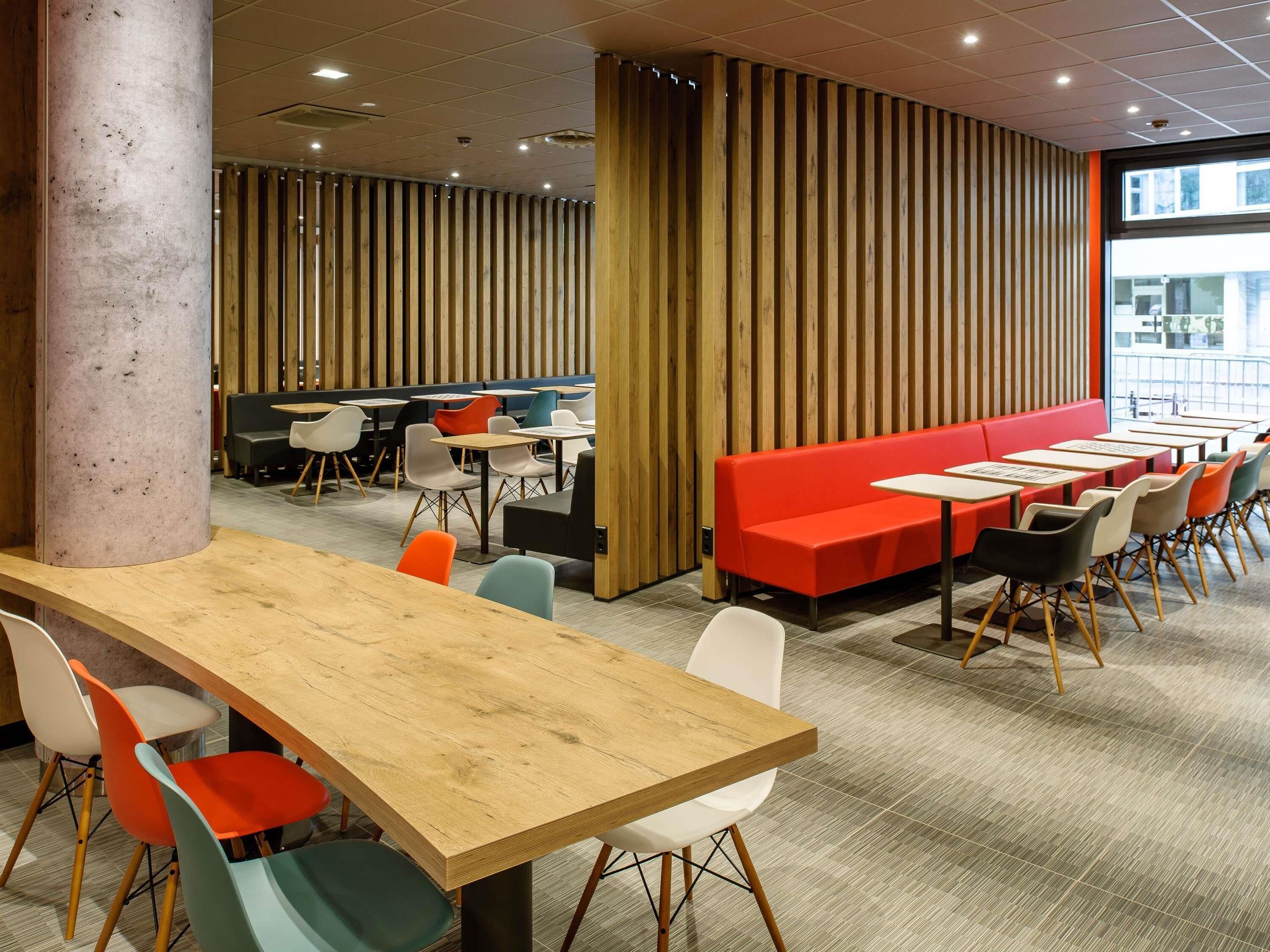 A modern dining area with a long wooden table, colorful chairs, and a red bench.