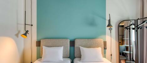 A hotel room with two single beds, a small table, a mirror, and a wardrobe.