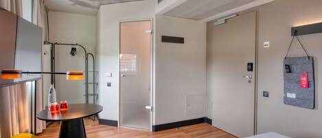 Una habitación de hotel moderna con una cama, una pequeña mesa redonda con sillas, un armario y una estación de carga en la pared.