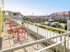 A balcony with red chairs and a table, overlooking a cityscape with buildings and a tower. - ibis Berlin Kurfürstendamm (Berlin)