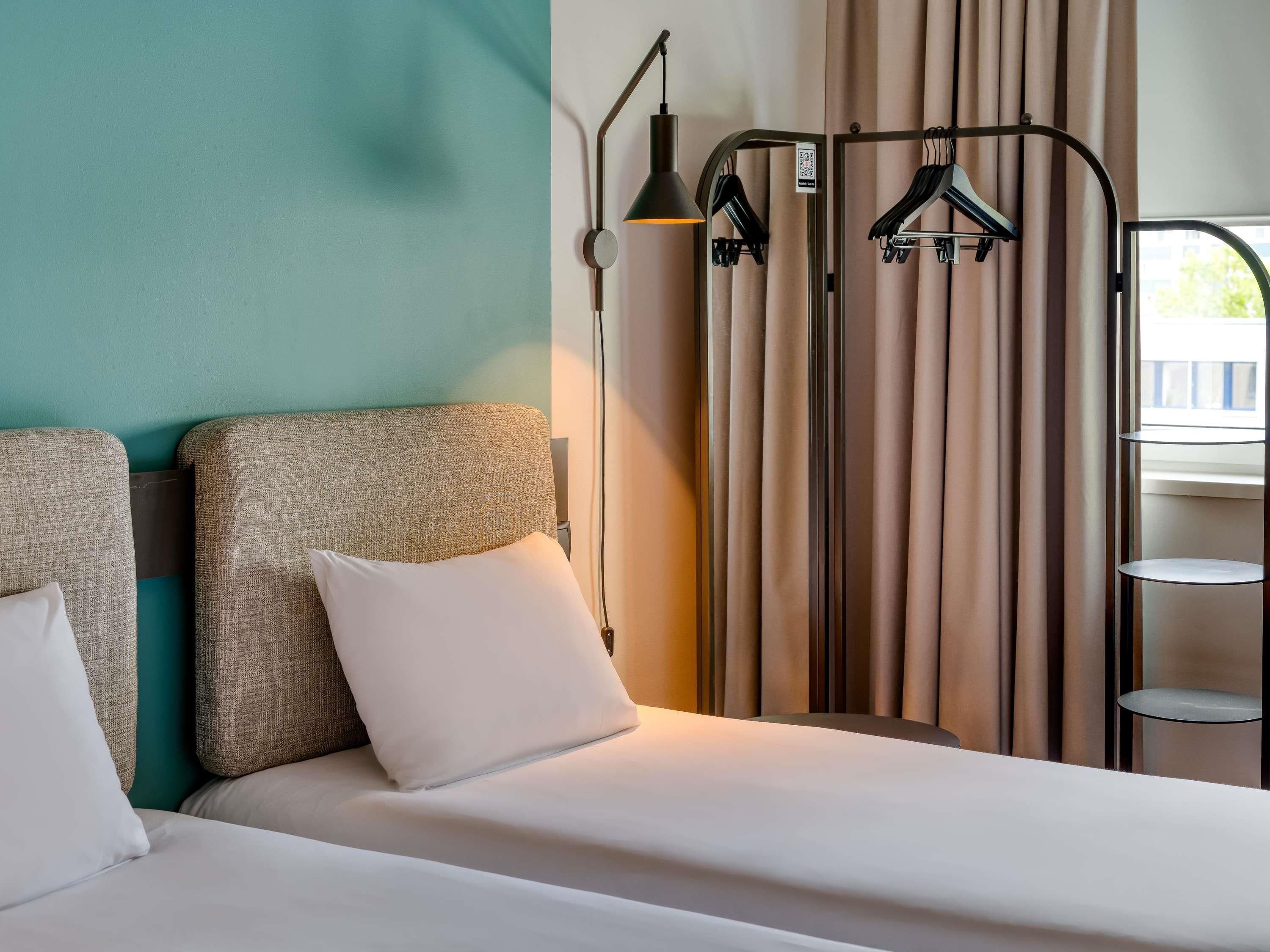 A hotel room with a bed, a hanging light fixture, and a window with curtains.