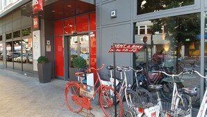 Un hotel con fachada roja y gris, servicio de alquiler de bicicletas y un cartel que ofrece alquiler de bicicletas por 1 día y 12 noches.