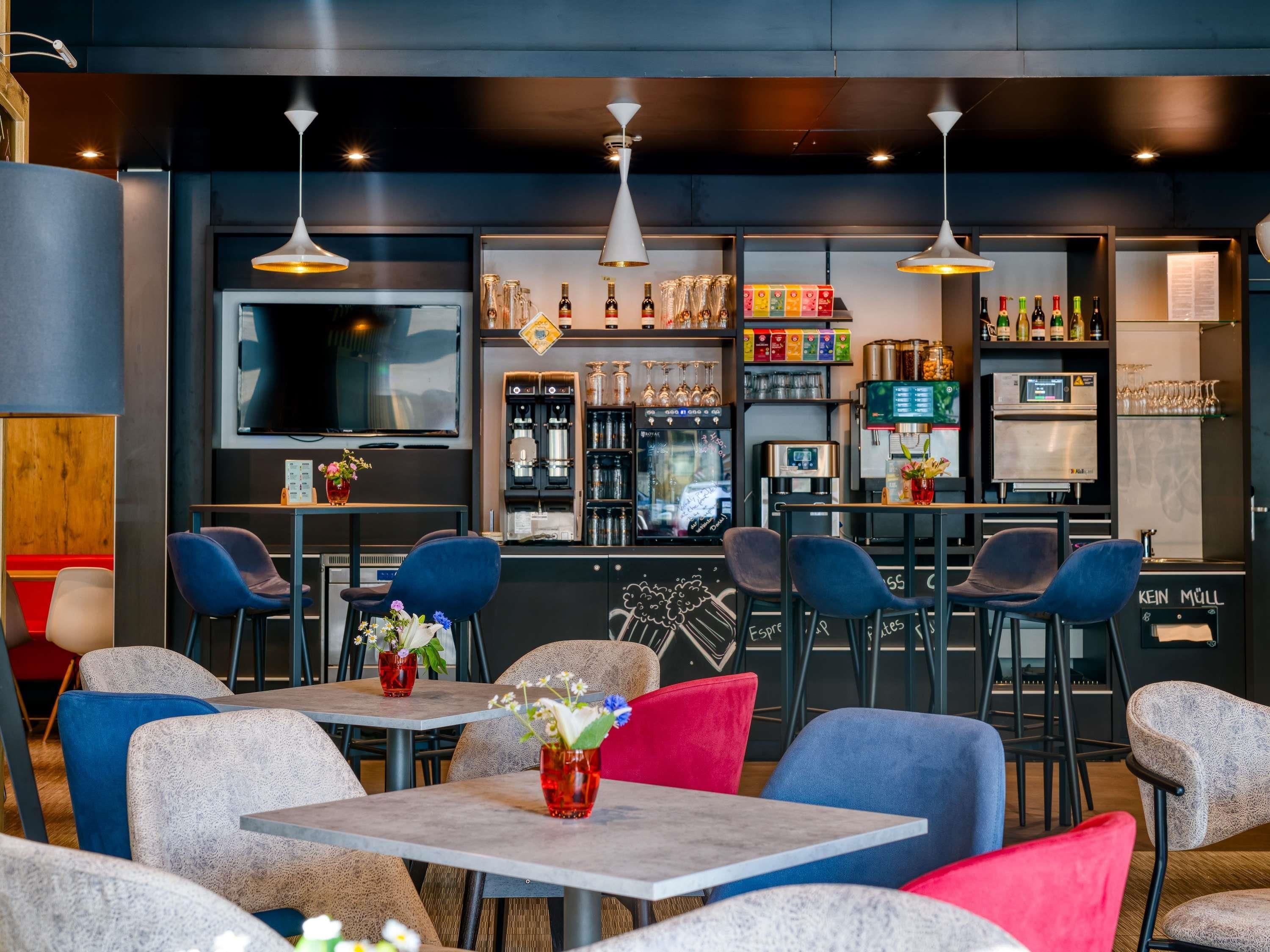 A modern bar area with seating, a coffee machine, and a variety of bottles and glasses.