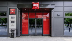 Exterior de un hotel ibis con diseño moderno, destacando una llamativa combinación de rojo y negro, amplias puertas de vidrio y una vista despejada del entorno.