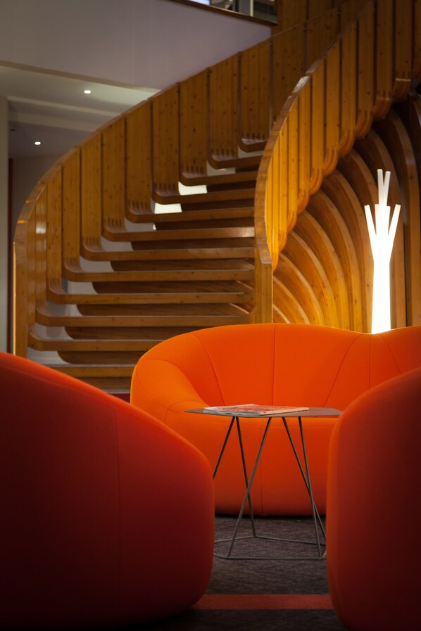 A modern interior with a curved wooden staircase and orange seating areas.