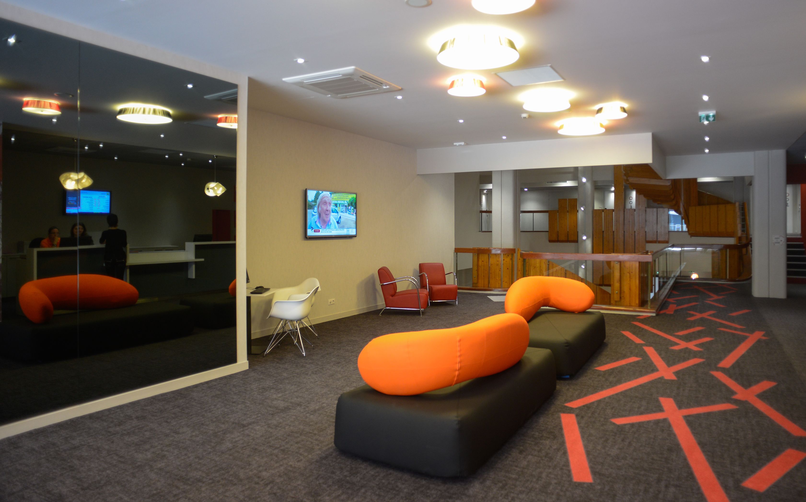 A modern lobby with a reception desk, seating area, and a staircase.