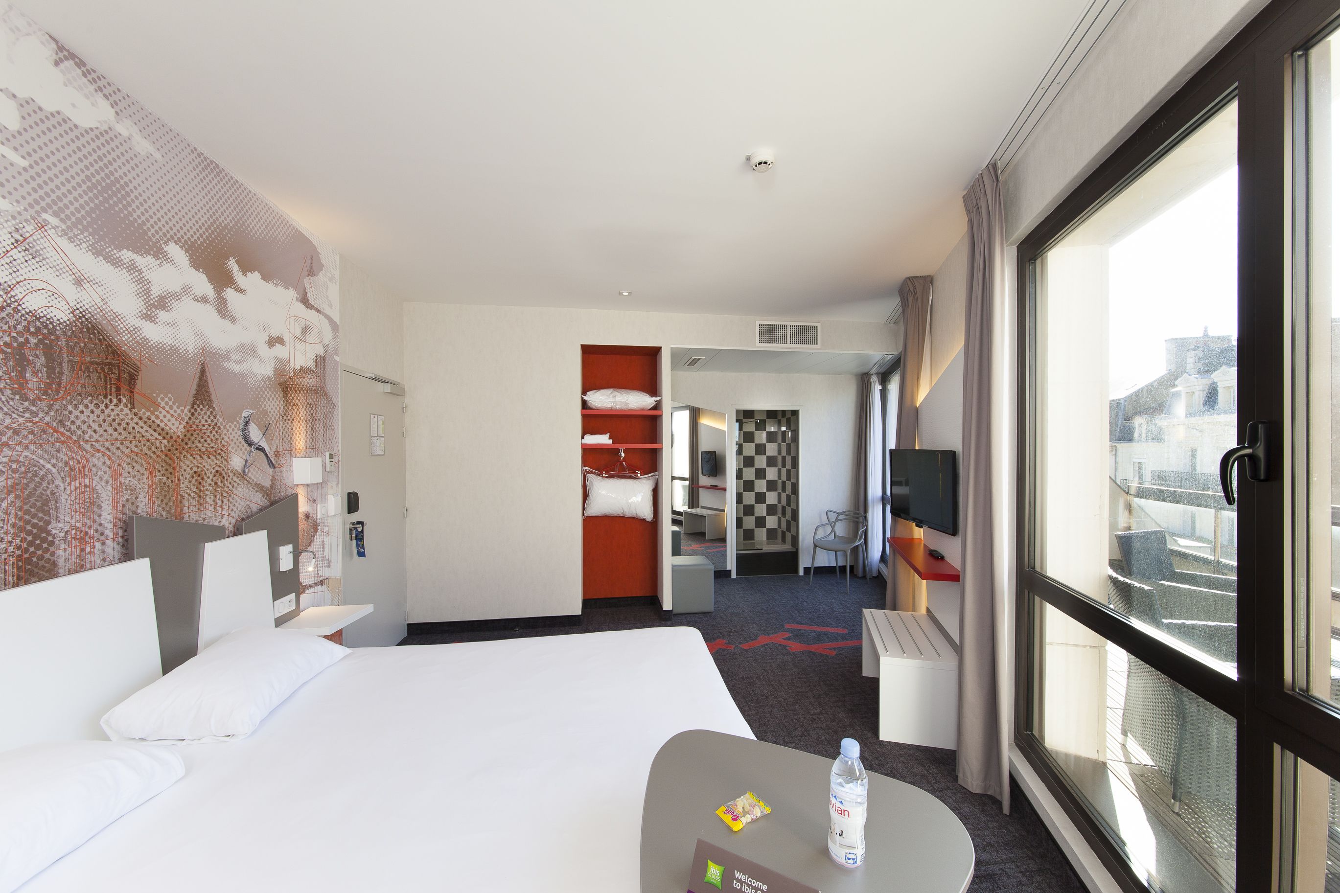 Habitación de hotel con una cama grande, un escritorio con silla, un televisor y ventana con vista a la ciudad.