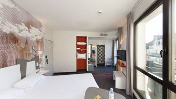 Habitación de hotel con una cama grande, un escritorio con silla, un televisor y ventana con vista a la ciudad.