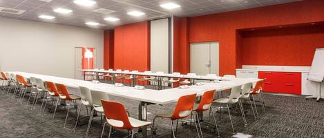 A conference room with a long table, multiple chairs, a whiteboard, and a red accent wall.