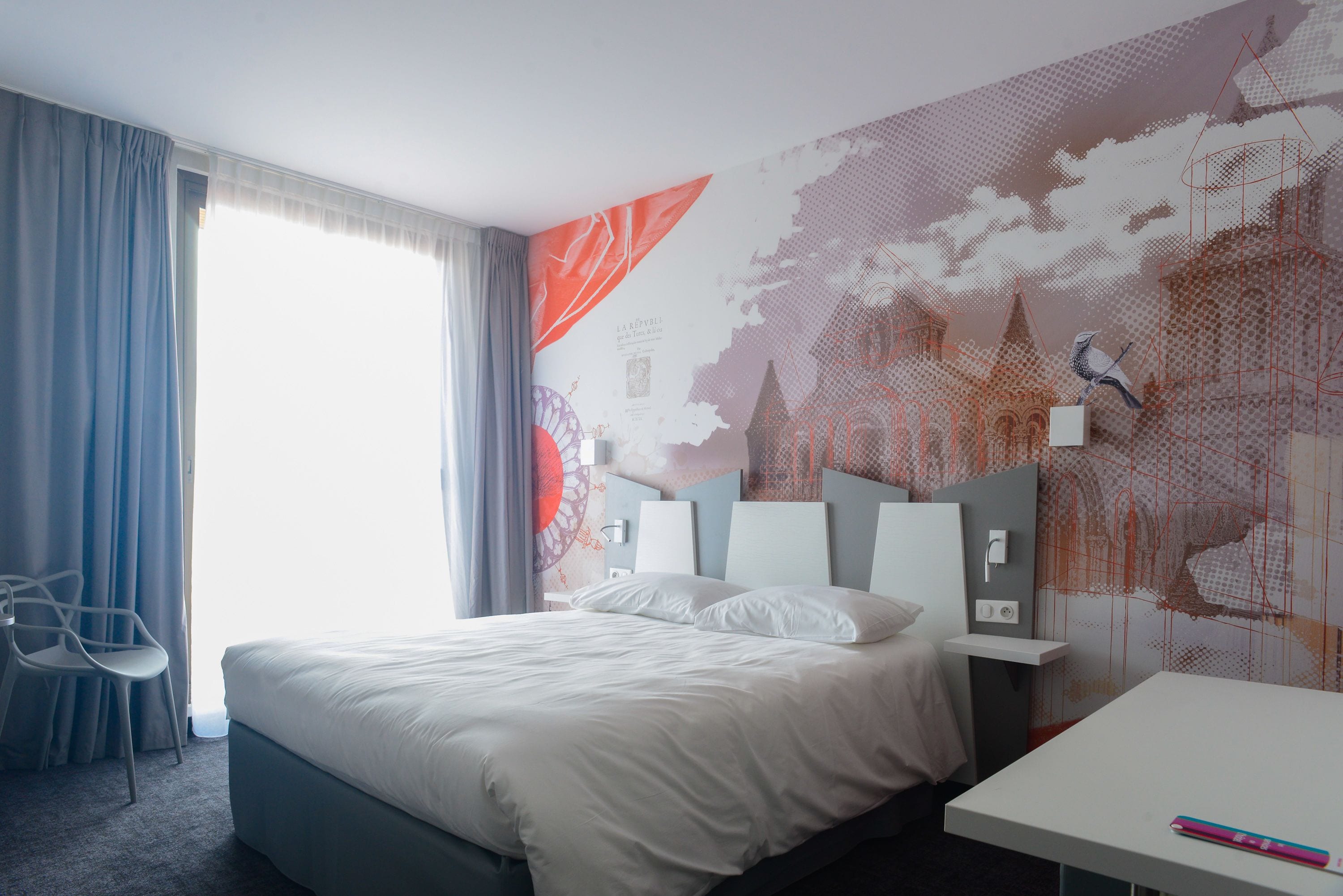 A modern hotel room with a large bed, a desk, and a chair.
