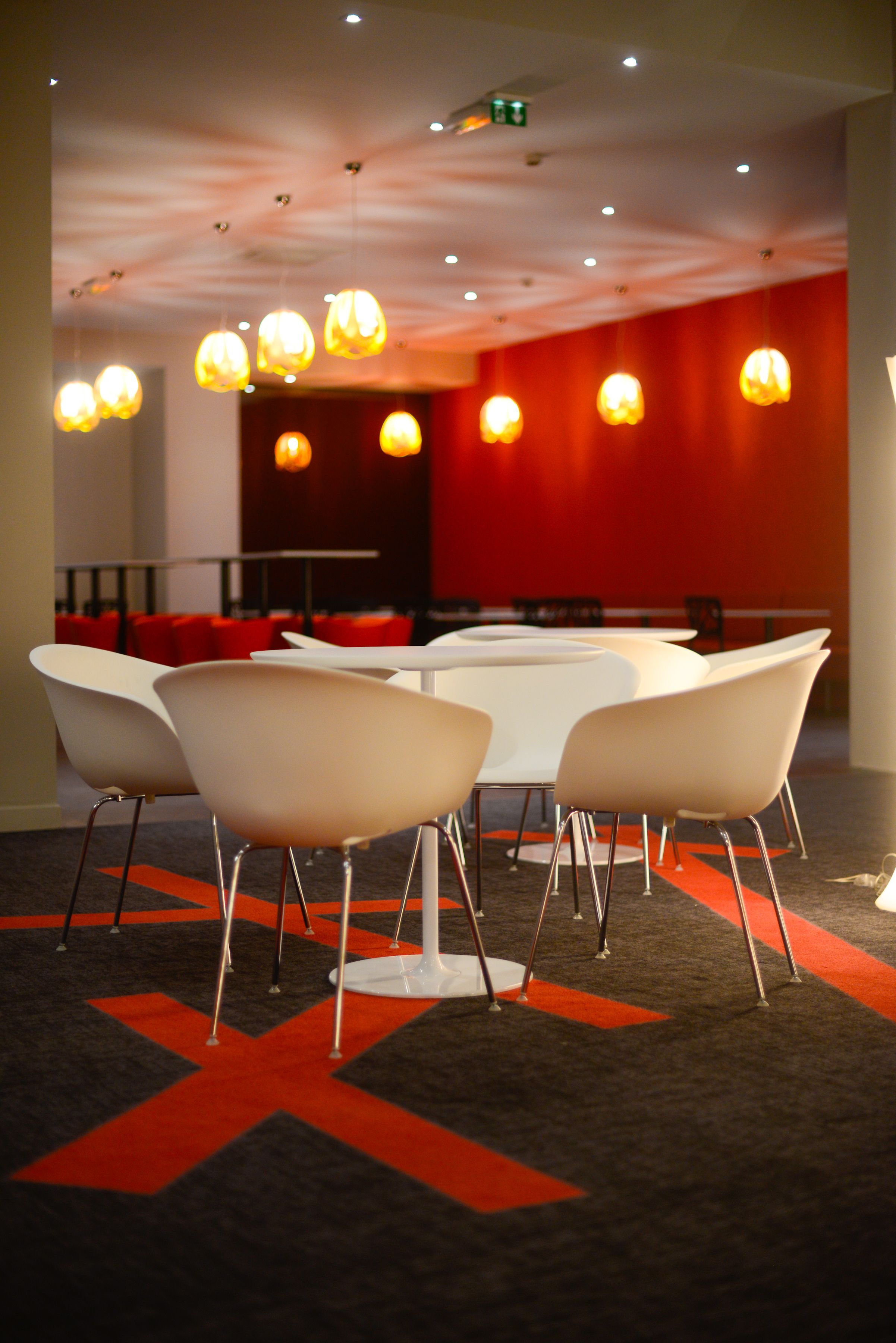 A conference room with white tables and chairs, red accents on the walls, and hanging pendant lights.