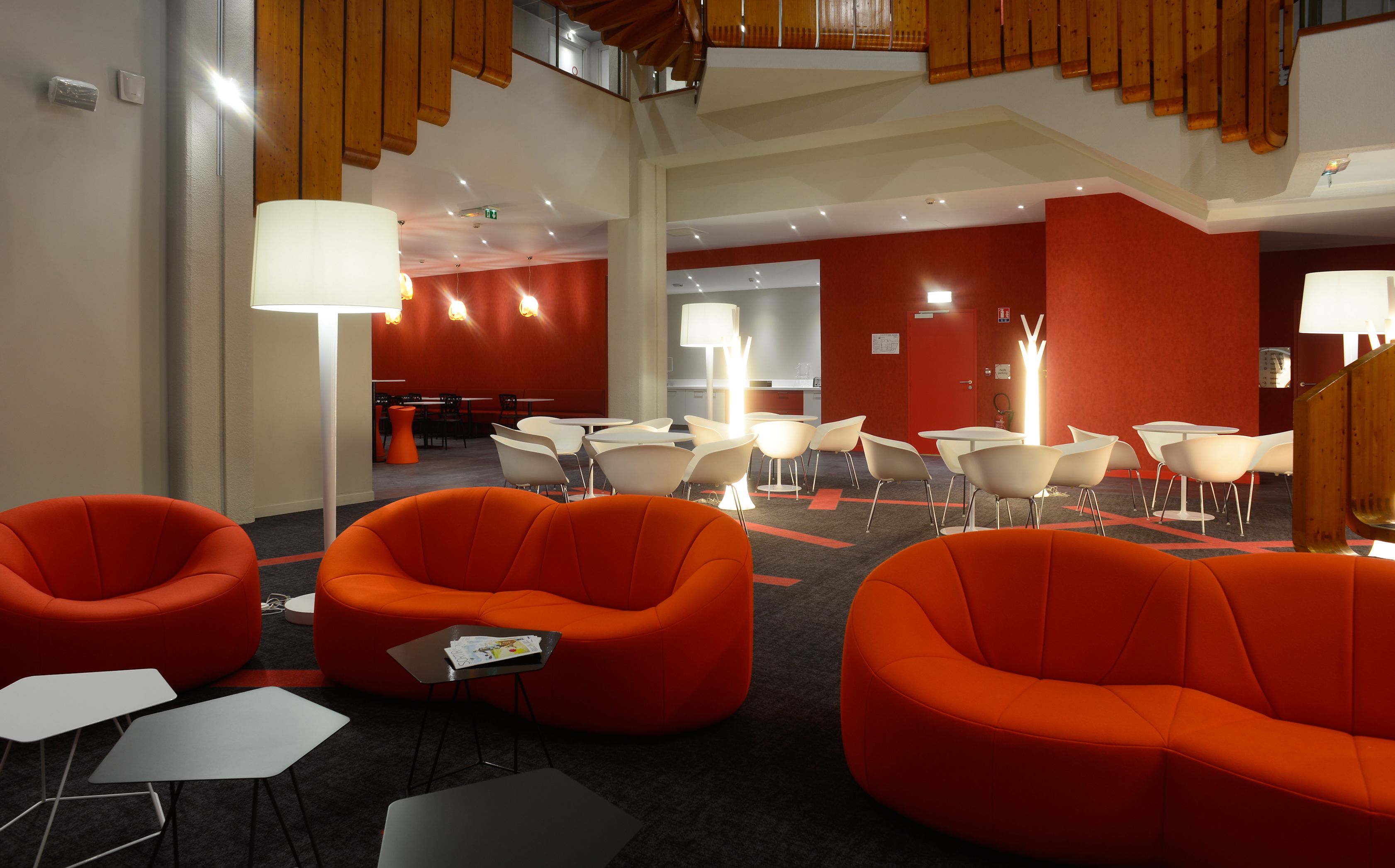 A modern hotel lobby with orange seating, white tables, and a staircase.