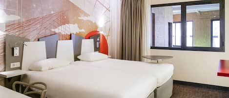 A hotel room with a large bed, a desk, a chair, a small table, and a window with curtains.