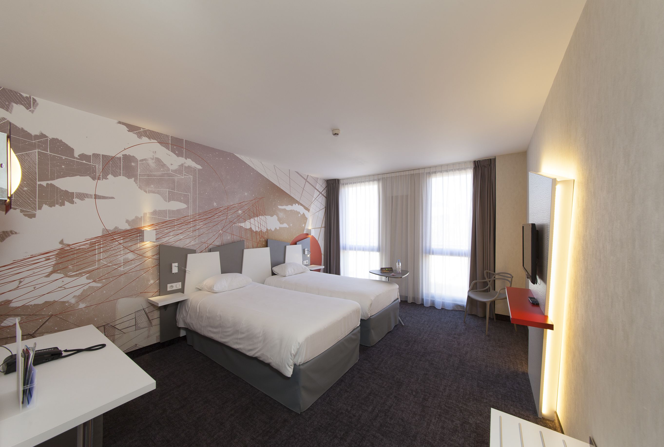 A hotel room with two beds, a desk, a chair, a TV, and a large window with curtains.